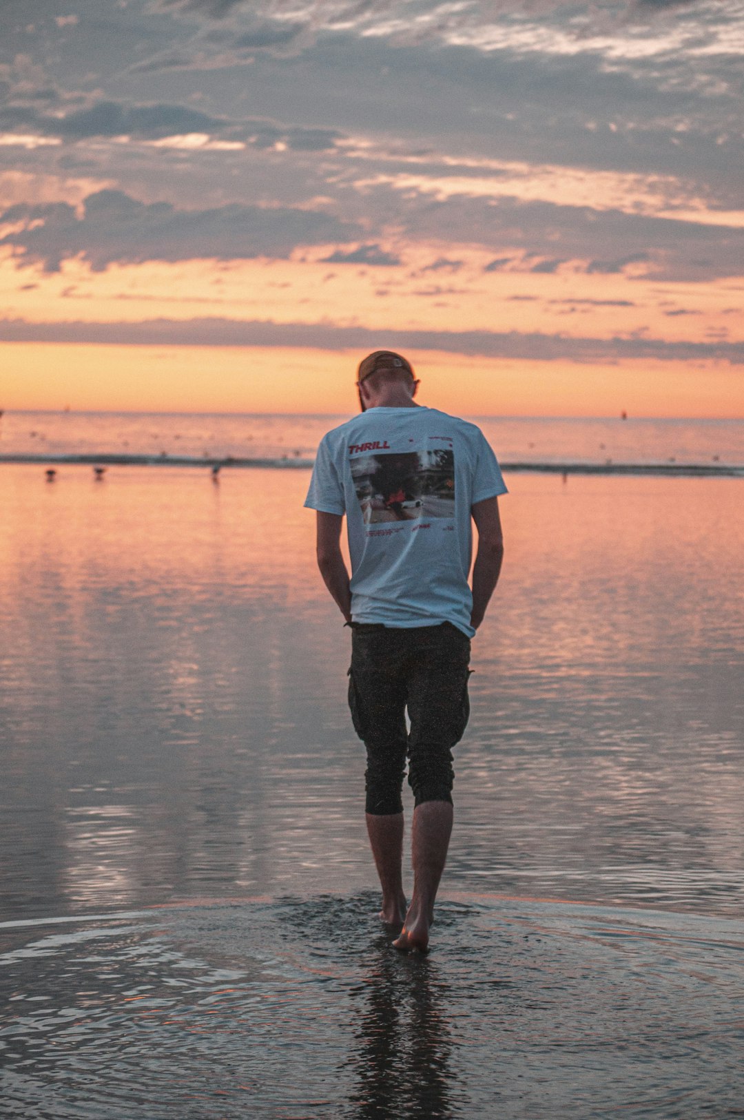 man in blue t-shirt and black shorts standing on water during sunset