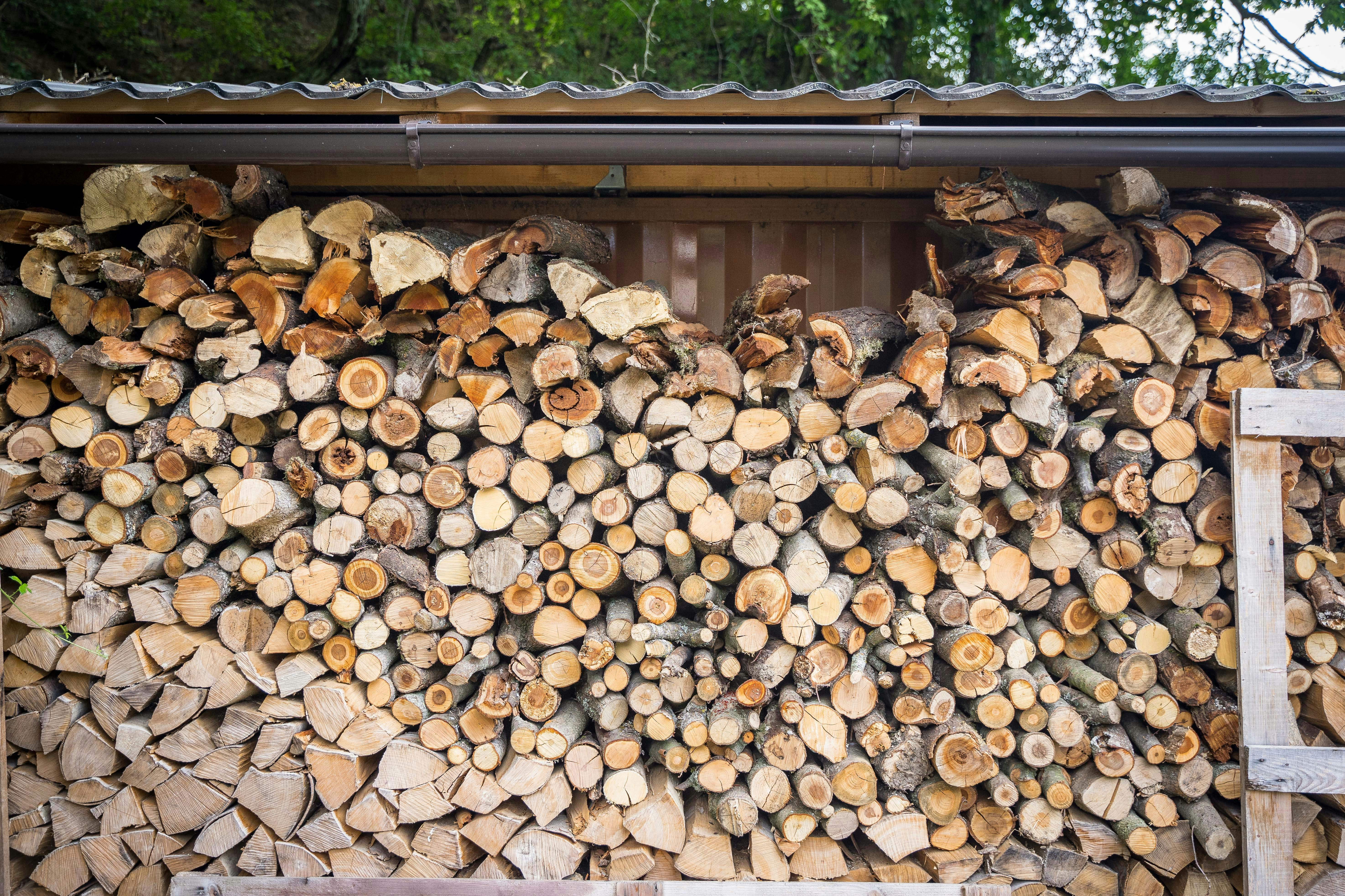 Split firewood stacked neatly under a wooden shelter roof.