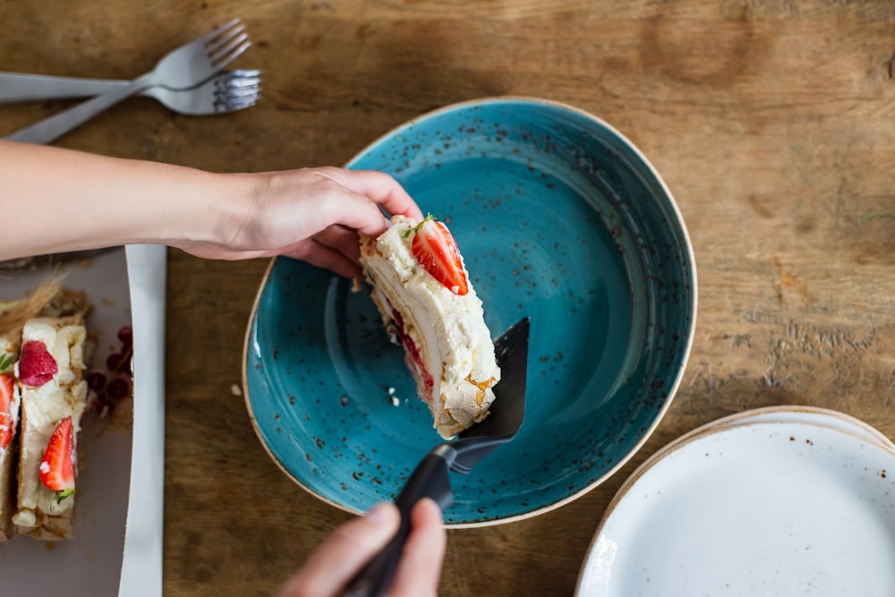 person holding blue ceramic bowl with stainless steel fork