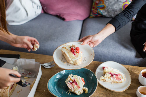 A smiling person holding a tray of assorted homemade cakes ready to share