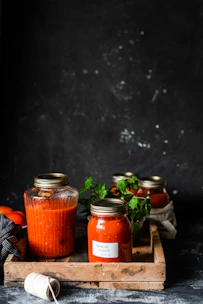 Bottles of rich, homemade sauces lined up with fresh herbs in the background.