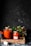Several jars filled with tomato sauce are arranged on a rustic wooden tray. The jars are sealed with metal lids. Fresh tomatoes and a small plant with green leaves are placed around the jars. The background is dark, creating a contrast with the vibrant red of the sauce.