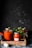 Several jars filled with tomato sauce are arranged on a rustic wooden tray. The jars are sealed with metal lids. Fresh tomatoes and a small plant with green leaves are placed around the jars. The background is dark, creating a contrast with the vibrant red of the sauce.