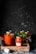 Several jars filled with tomato sauce are arranged on a rustic wooden tray. The jars are sealed with metal lids. Fresh tomatoes and a small plant with green leaves are placed around the jars. The background is dark, creating a contrast with the vibrant red of the sauce.