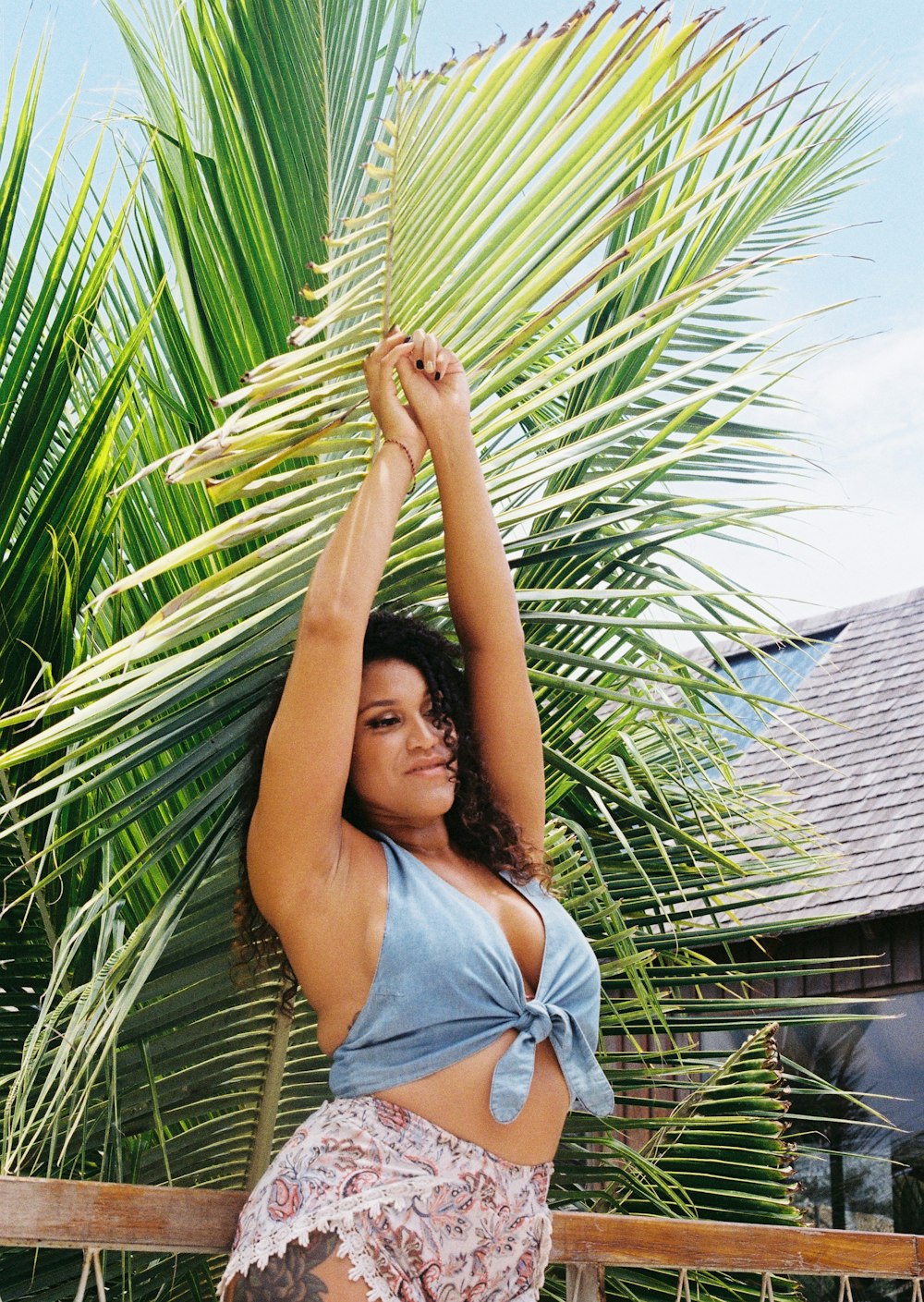 woman in blue tank top and blue denim shorts standing under palm tree during daytime