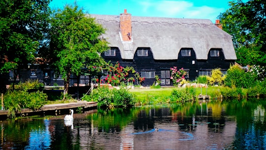 brown concrete building near green trees and river during daytime in Flatford: Bridge Cottage United Kingdom