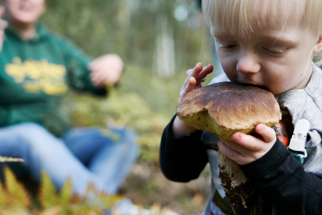 child in white and black long sleeve shirt holding brown mushroom during daytime