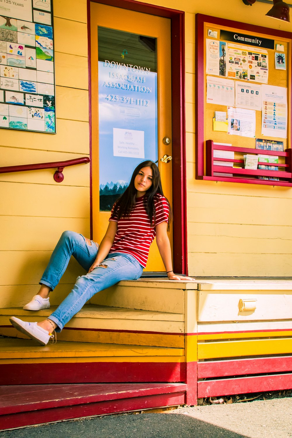 woman in black and white striped shirt and blue denim jeans sitting on brown wooden desk