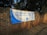 A large white and blue banner is stretched across a brick wall. The banner reads 'ELECTORAL COMMISSION ENSURING FREE AND FAIR ELECTIONS' with the logo of the Independent Electoral Commission of South Africa in the center. The surrounding area is shaded by trees.