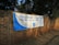A large white and blue banner is stretched across a brick wall. The banner reads 'ELECTORAL COMMISSION ENSURING FREE AND FAIR ELECTIONS' with the logo of the Independent Electoral Commission of South Africa in the center. The surrounding area is shaded by trees.