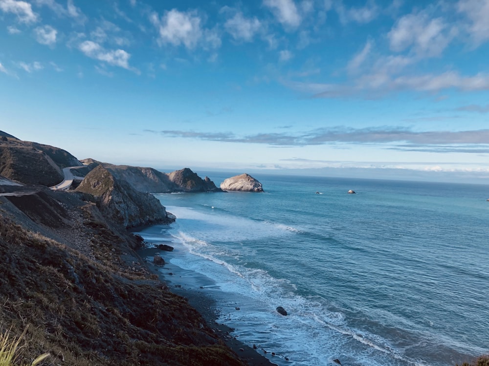 brown rocky mountain beside blue sea under blue sky during daytime