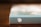 A canvas with a blue-green border sits on a wooden surface. On the side of the canvas, there is a white illustration of a ladybug.