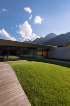 brown wooden house on green grass field near mountain under white clouds during daytime