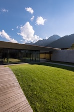 brown wooden house on green grass field near mountain under white clouds during daytime