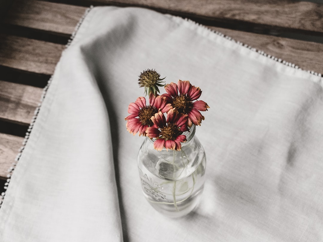 white and yellow flower in clear glass vase on white textile