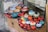 A display of colorful ceramic bowls and decorative items resembling pomegranates are arranged on a raised surface. The objects feature intricate patterns and vibrant colors, including red, blue, orange, and turquoise. They are placed on top of cardboard packaging with labels indicating fragility.