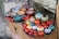 A display of colorful ceramic bowls and decorative items resembling pomegranates are arranged on a raised surface. The objects feature intricate patterns and vibrant colors, including red, blue, orange, and turquoise. They are placed on top of cardboard packaging with labels indicating fragility.