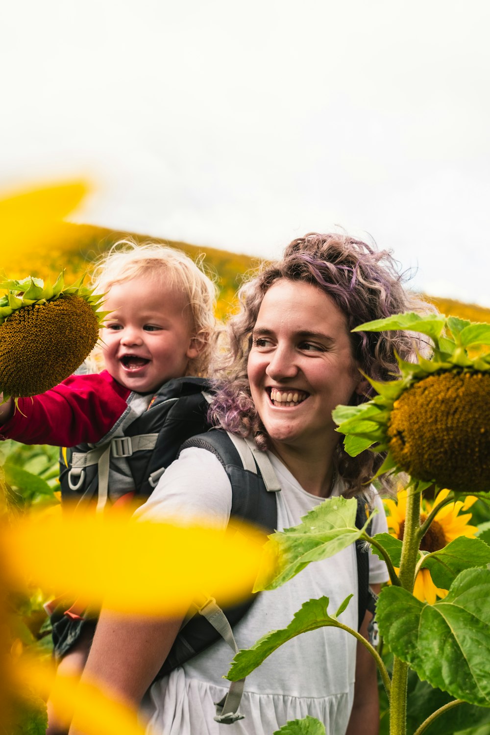 woman in white shirt carrying baby in yellow sunflower field during daytime
