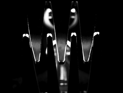 Close-up black and white image of a fork, focusing on two shiny prongs that create dramatic shadows and reflections against a dark background.