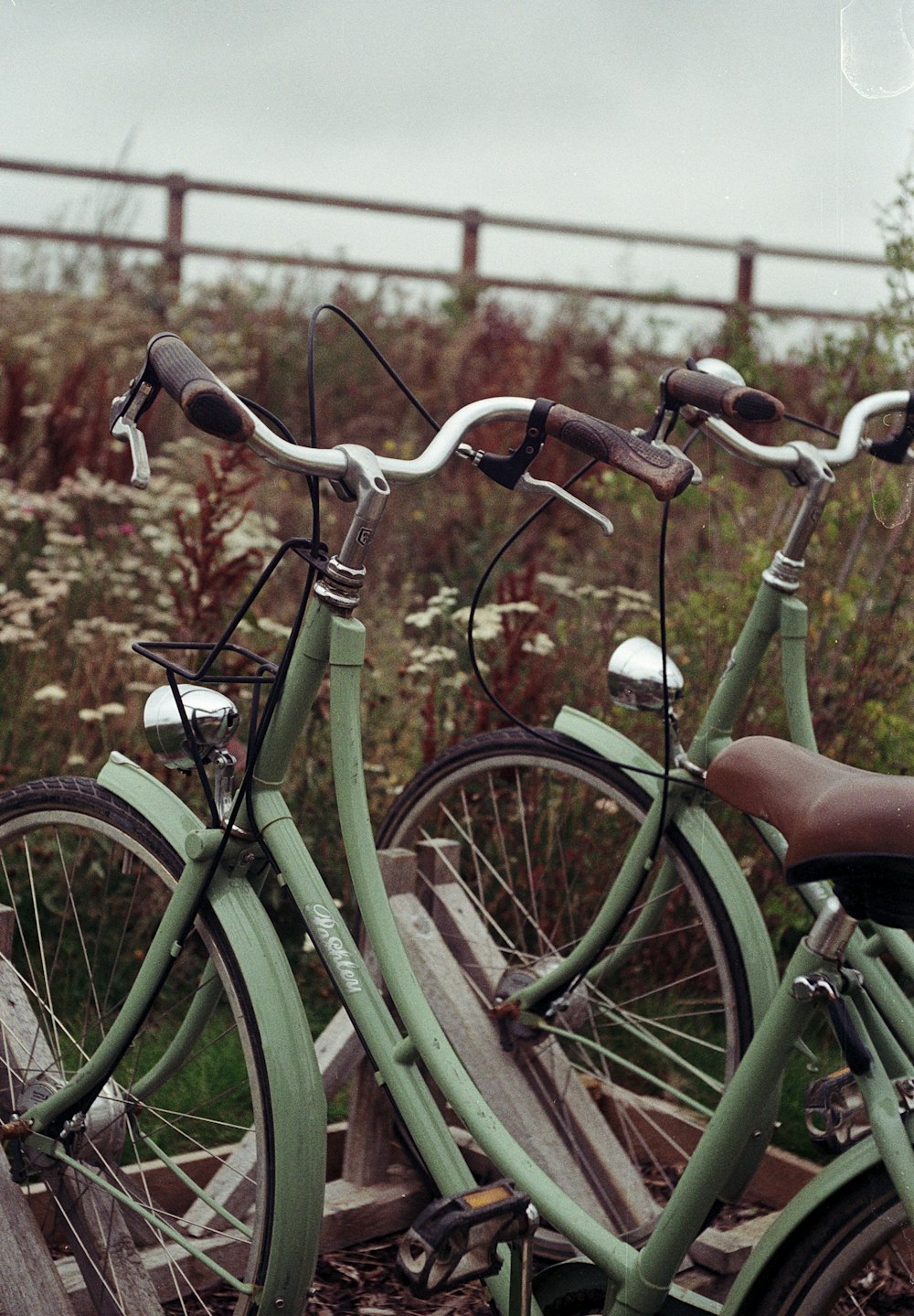 green city bike parked beside brown wooden fence