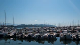 A spacious motorboat docked at a bustling marina with mountains in the background.