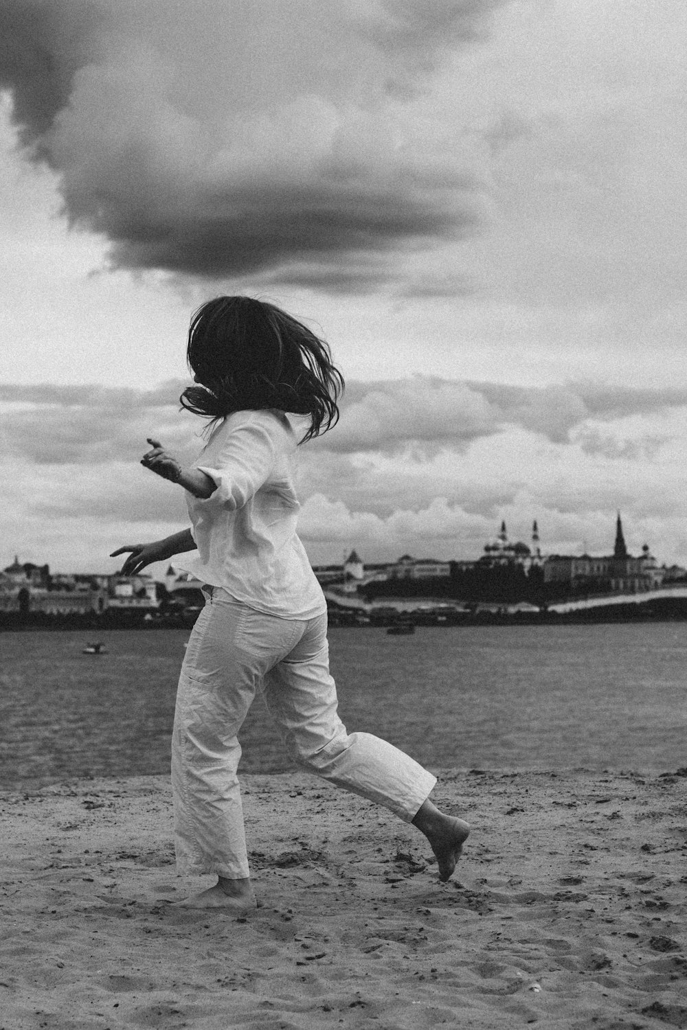 grayscale photo of woman in white long sleeve shirt and pants standing on seashore