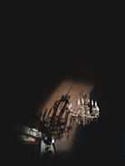 A black wrought iron chandelier adorned with crystals hanging in a shadowy room.