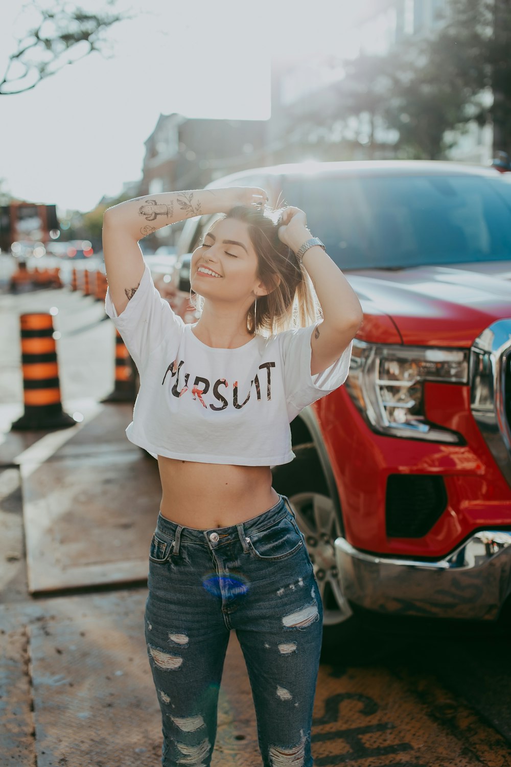 woman in white and black crop top and blue denim shorts standing near red car