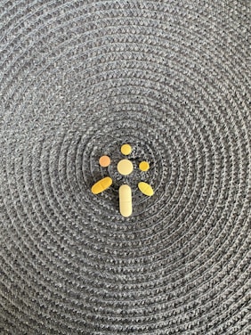 A collection of various shaped pills and tablets is arranged on a woven, textured surface with a circular pattern.