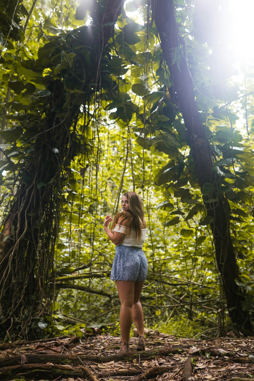 girl in white tank top and blue denim shorts standing on brown wooden swing under green