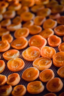 Halved apricots arranged on a drying rack, showcasing their vibrant orange hues and textured interiors. The close-up perspective highlights the freshness and natural details of the fruit.