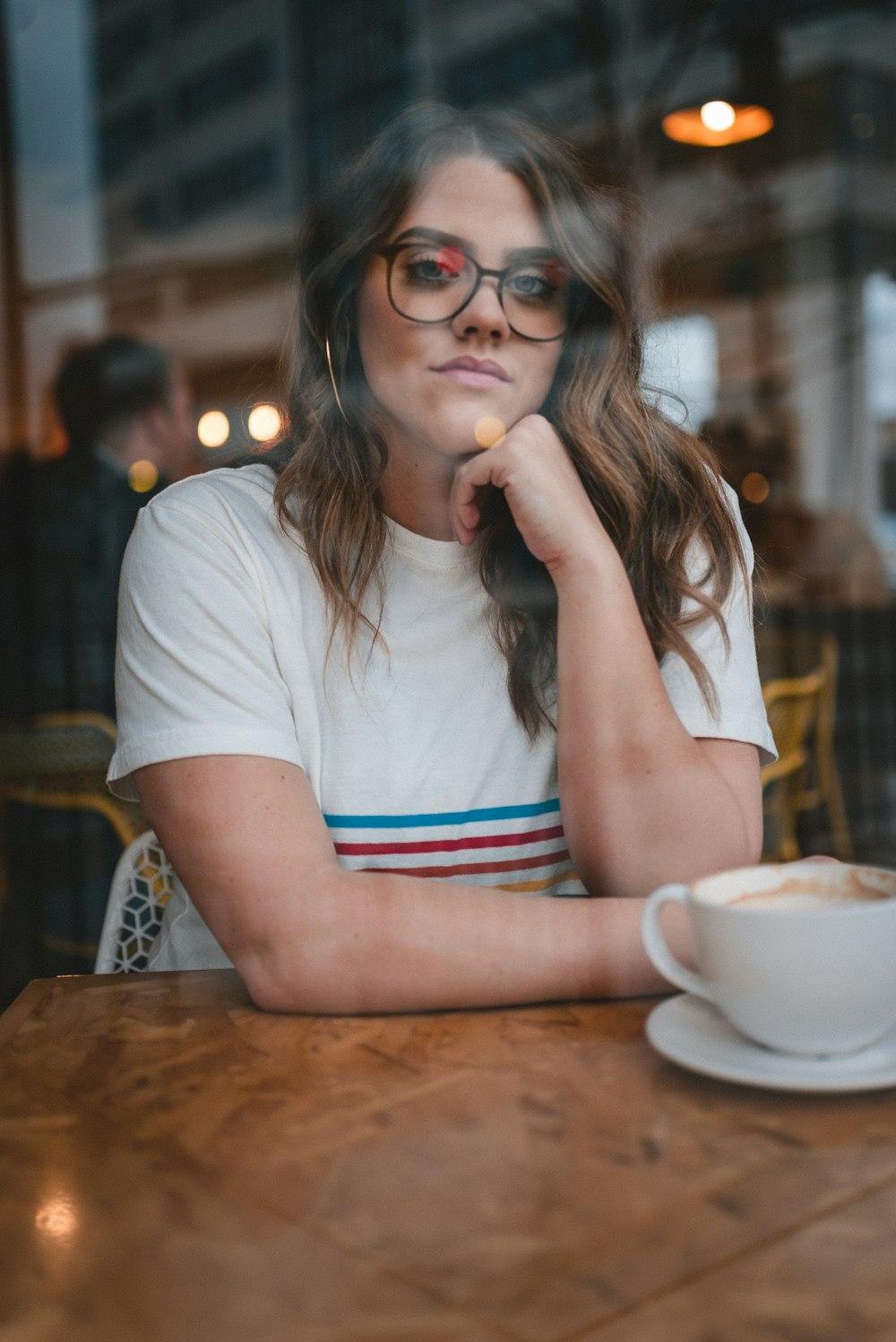 Mujer con camiseta blanca de cuello redondo con gafas de montura negra sentada a la mesa