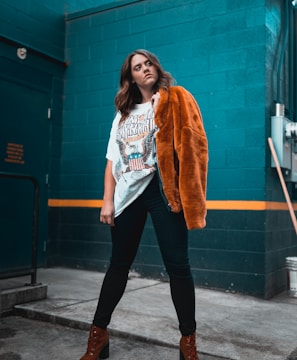 woman in white shirt and orange coat standing beside blue wall