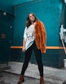 woman in white shirt and orange coat standing beside blue wall