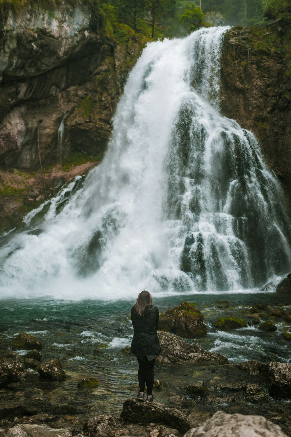 man in black jacket standing on rock near waterfalls during daytime