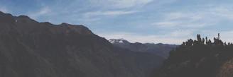 A panoramic mountain view with hikers pausing to admire the vast landscape under a clear blue sky.