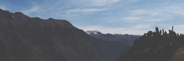 A panoramic mountain view with hikers pausing to admire the vast landscape under a clear blue sky.