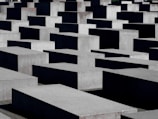 Numerous large concrete slabs are arranged in a grid-like pattern. The structures vary slightly in height, creating a visually striking geometric landscape. The shadows cast by the blocks add depth to the scene.