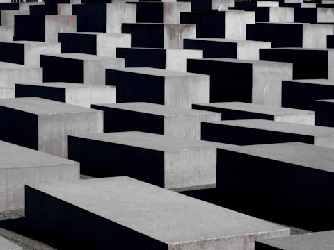 Numerous large concrete slabs are arranged in a grid-like pattern. The structures vary slightly in height, creating a visually striking geometric landscape. The shadows cast by the blocks add depth to the scene.