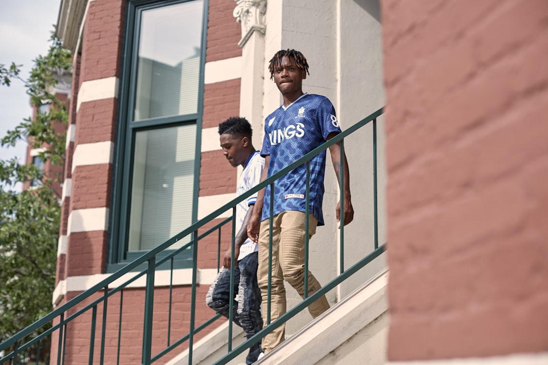 man in blue and white crew neck t-shirt and brown pants standing on black metal