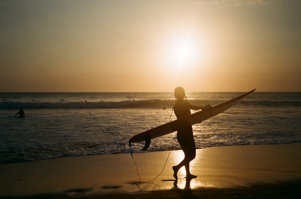 silhouette of man holding surfboard on beach during sunset