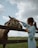 Young woman visiting the farm, gently petting a buffalo under clear blue skies.