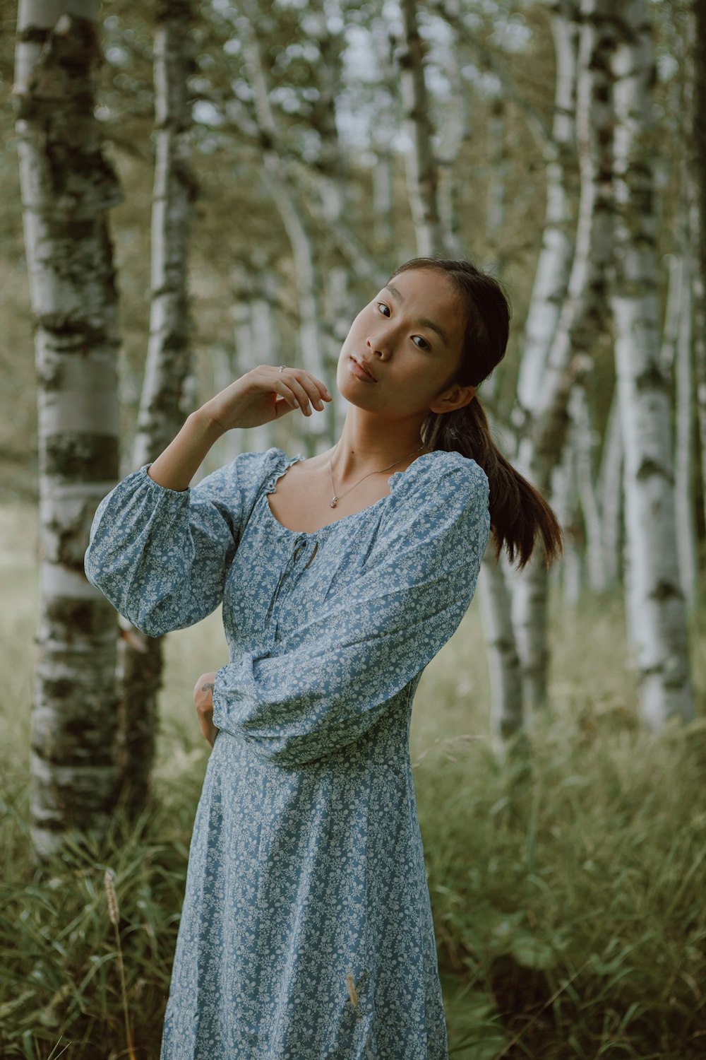 woman in gray long sleeve dress standing on green grass field during daytime