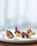 A gourmet dish is artfully presented on a plate with succulent pieces of meat garnished with colorful sauces and edible flowers. The dish includes vibrant splashes of red and yellow, complemented by green herbs, creating an elegant and sophisticated culinary presentation.