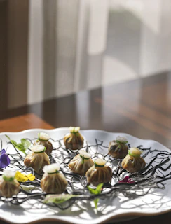 Delicate mantu dumplings topped with a light tomato sauce and yogurt, styled with rounded corners and soft shadows on a minimal cream backdrop.