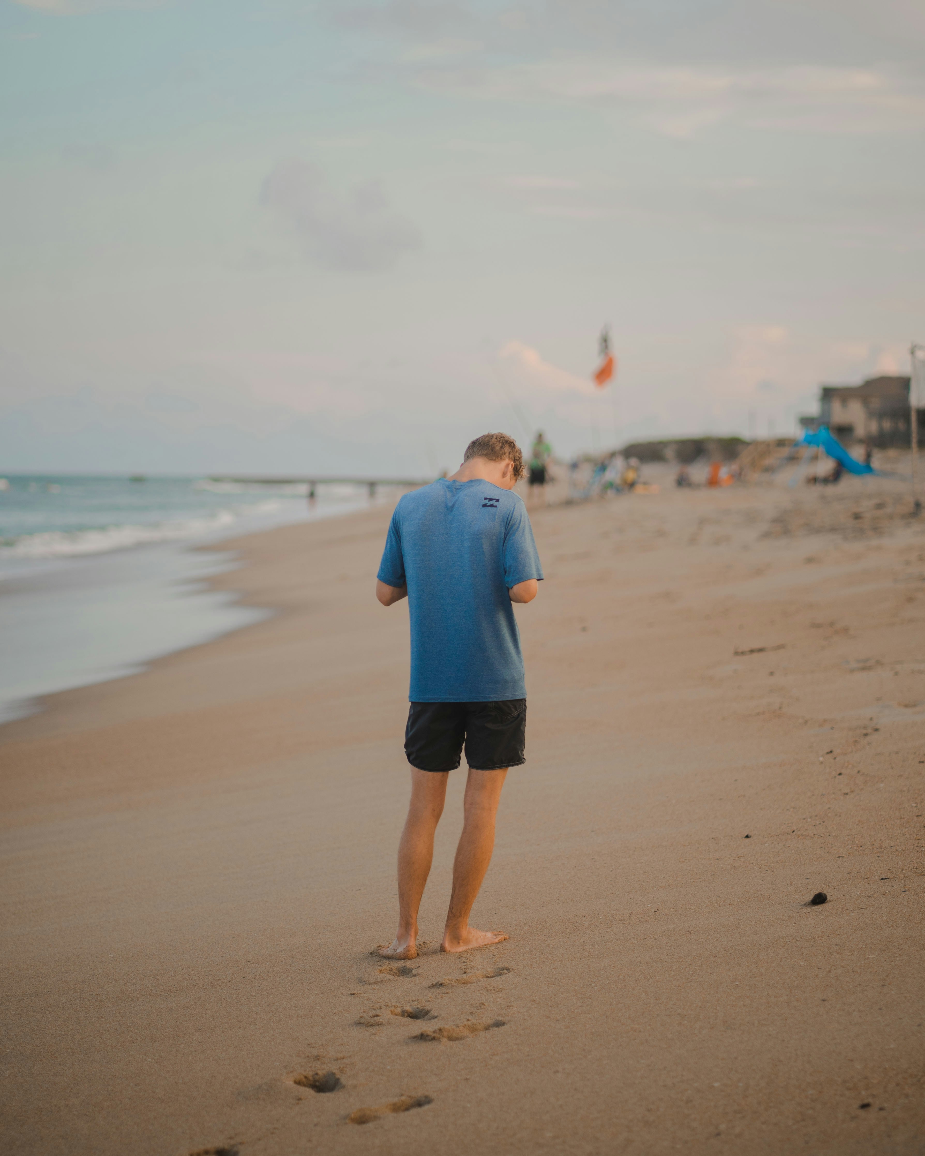 man in blue dress shirt and black shorts walking on beach during daytime