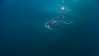 An aerial view of a small stretch of islands surrounded by vast expanses of deep blue water. The islands have a rugged coastline with patches of greenery and sandy beaches. A few wisps of clouds are visible above the water, adding to the serene atmosphere.
