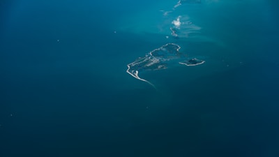 An aerial view of a small stretch of islands surrounded by vast expanses of deep blue water. The islands have a rugged coastline with patches of greenery and sandy beaches. A few wisps of clouds are visible above the water, adding to the serene atmosphere.