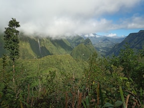 green grass field near mountain under white clouds during daytime