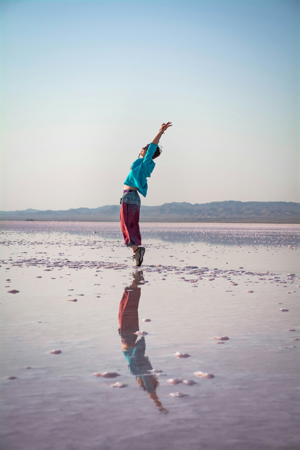 woman in blue jacket and red pants standing on seashore during daytime